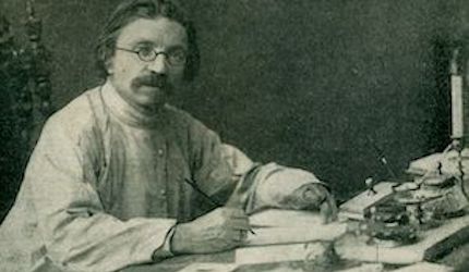 Middle aged man with round eye glasses sitting at a writing desk